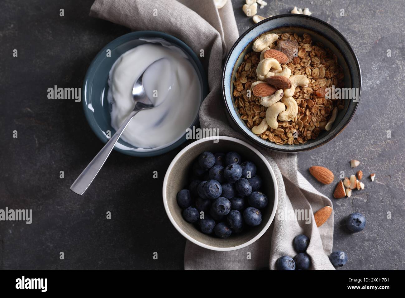 Tasty granola in bowl, blueberries, yogurt and spoon on gray textured table, flat lay Stock Photo