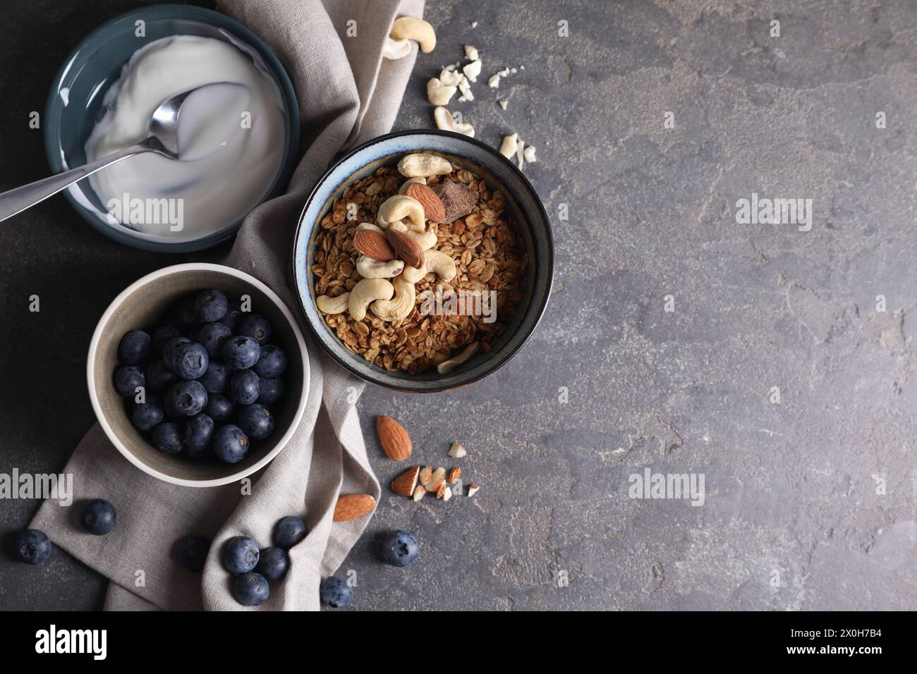 Tasty granola in bowl, blueberries, yogurt and spoon on gray textured table, flat lay. Space for text Stock Photo