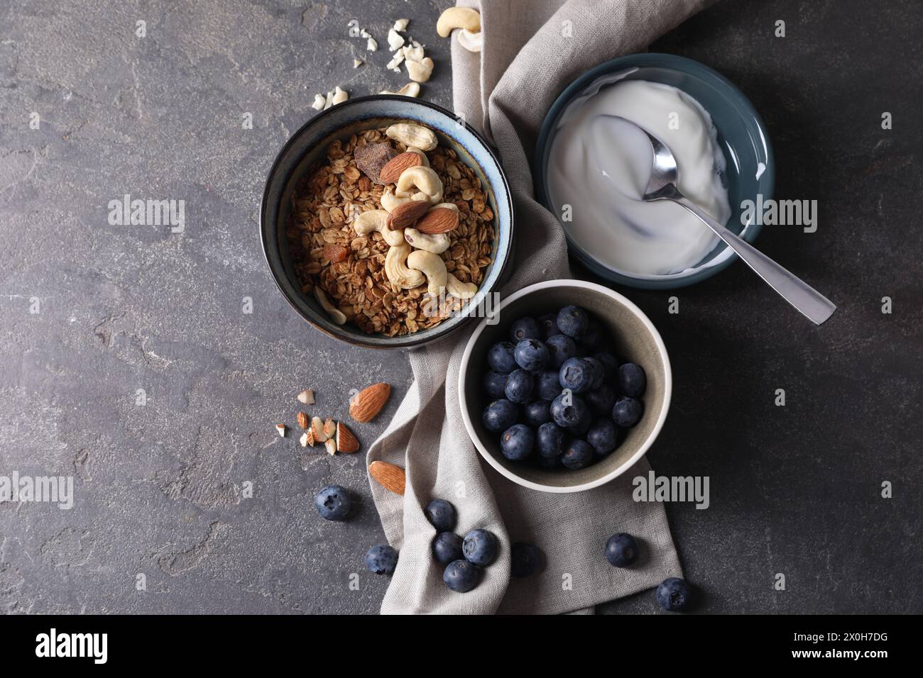 Tasty granola in bowl, blueberries, yogurt and spoon on gray textured table, flat lay. Space for text Stock Photo