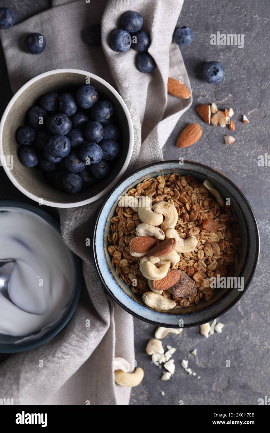 Tasty granola in bowl, blueberries and yogurt on gray textured table, flat lay Stock Photo