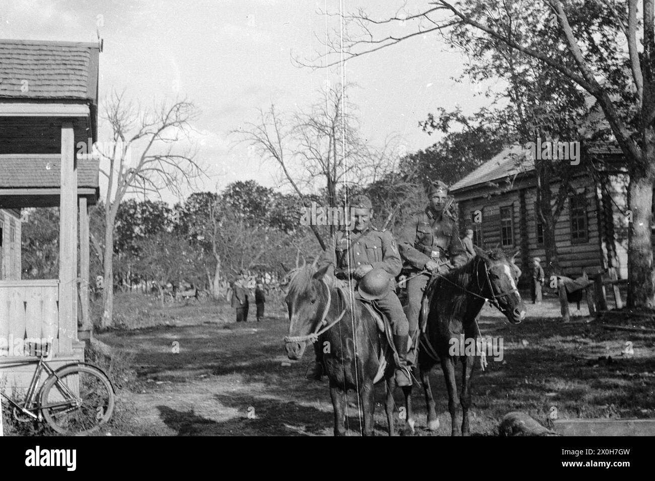 German soldiers ride horses in a village. Children are playing in the background. The picture was taken by a member of the Radfahrgrenadierregiment 2 / Radfahrsicherungsregiment 2, on the Eastern Front. [automated translation] Stock Photo
