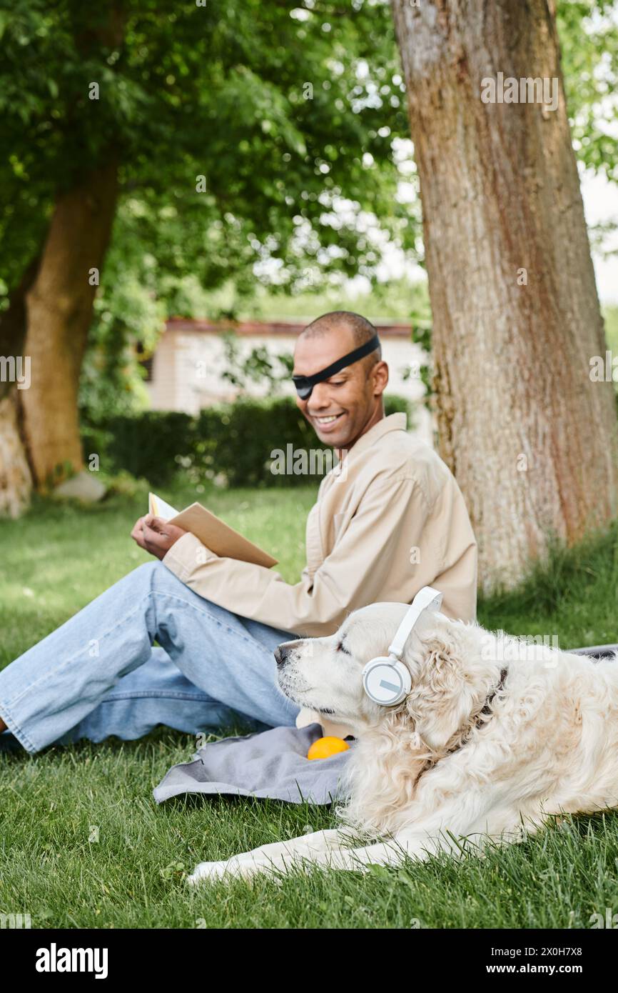 A man with myasthenia gravis syndrome sits with his Labrador dog in the grass, both wearing headphones. Stock Photo