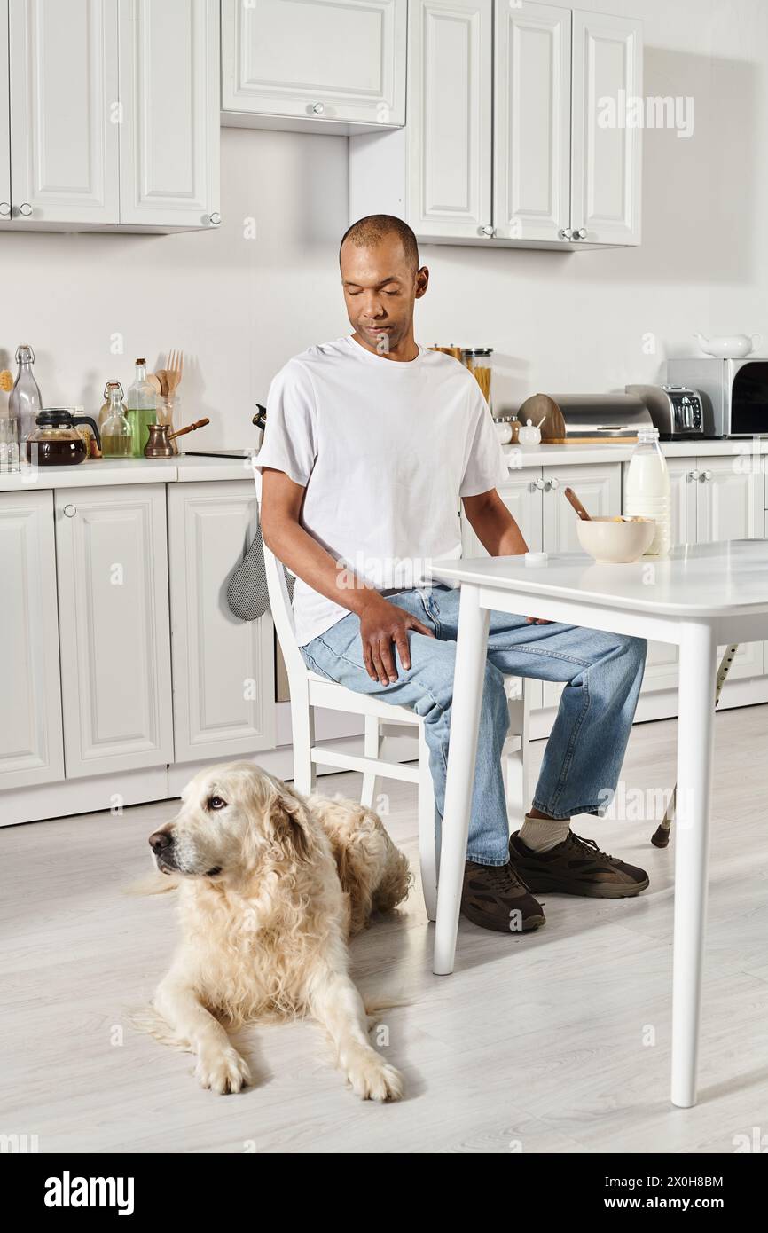 A disabled African American man sits at a kitchen table next to a Labrador dog, fostering a heartwarming connection. Stock Photo