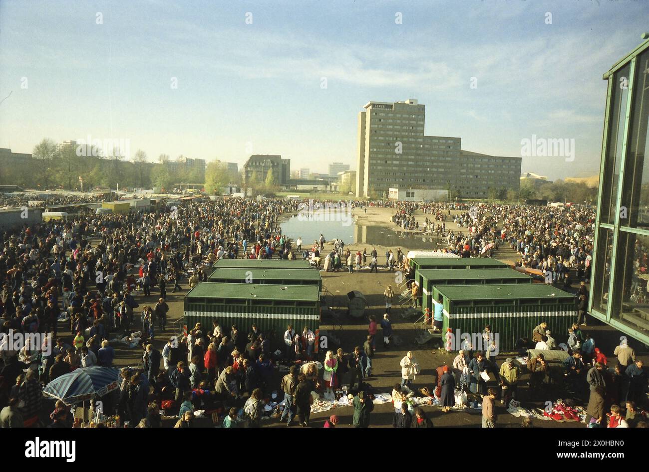 A crowd of people stand around a puddle of water and containers on the ...