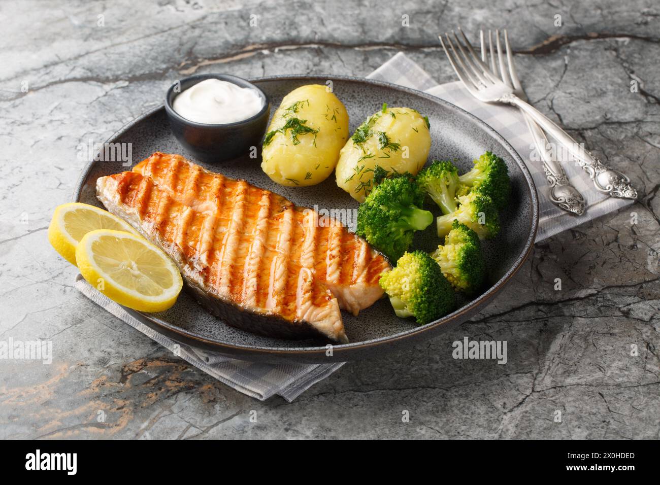 Grilled salmon, boiled potatoes, broccoli and cream sauce in a plate on the table. Horizontal Stock Photo
