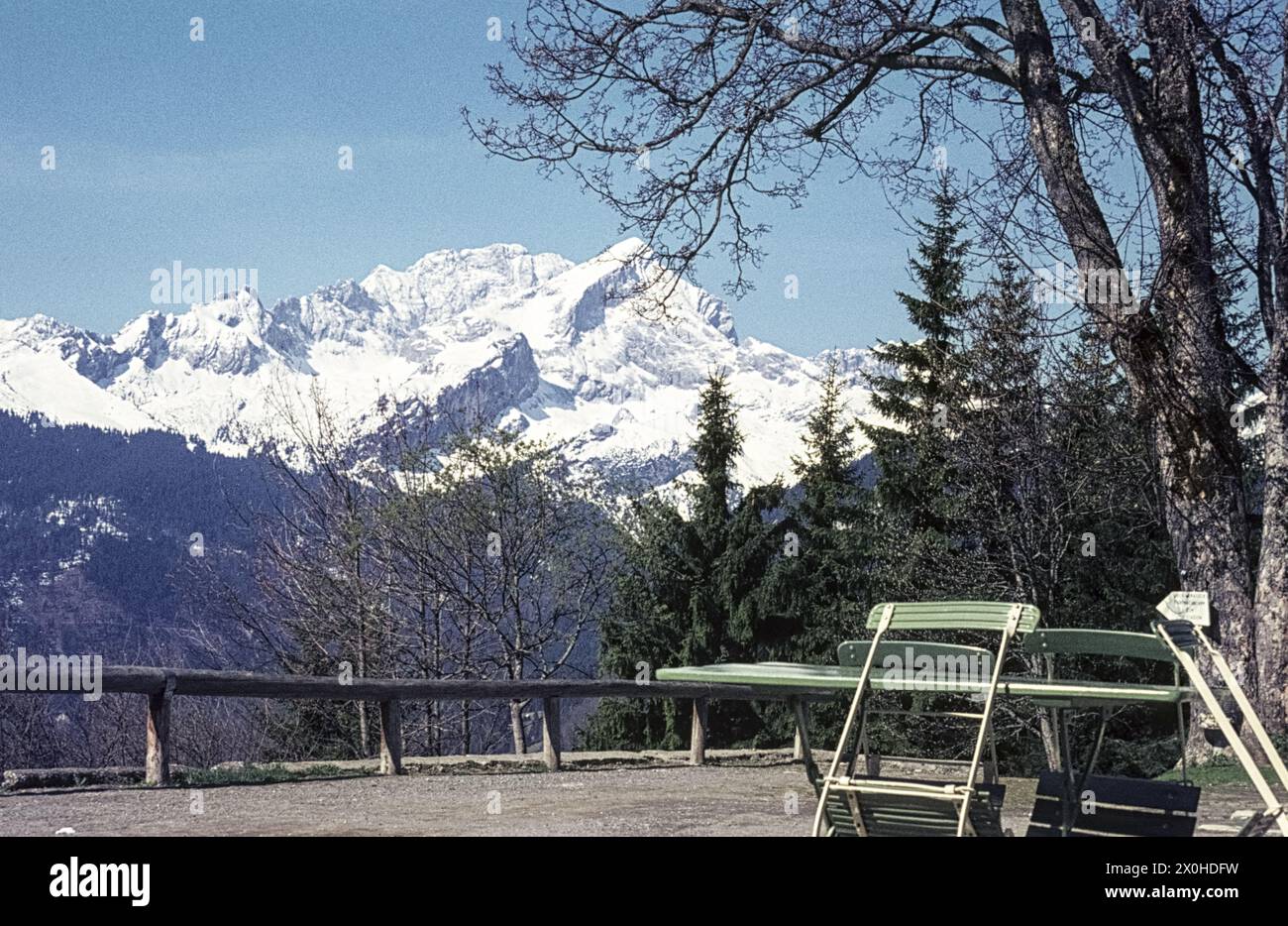 View of the snow-covered Alpspitze from Berggasthof Eckbauer, green chairs leaning against a table. [automated translation] Stock Photo