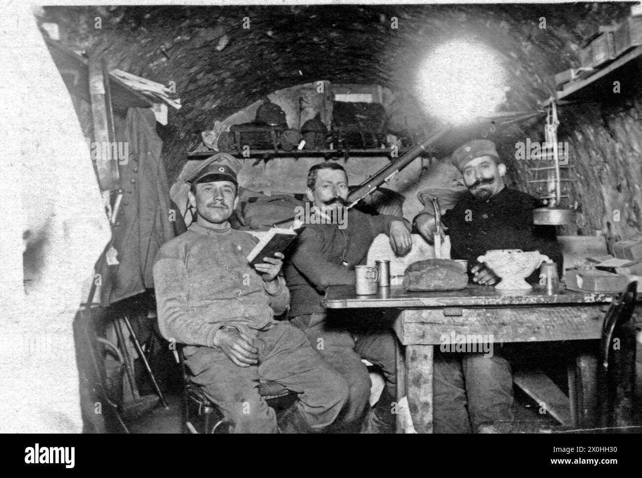 Drei Soldaten in einem Bunker, sehr wahrscheinlich an der französischen Grenze während des Ersten Weltkrieges. Auf dem Tisch steht Verpflegung, im Hintergrund liegt ein Gewehr und im Regal an der Wand die Pickelhauben. (Aufnahmedatum: 01.01.1914-31.12.1914) Stock Photo
