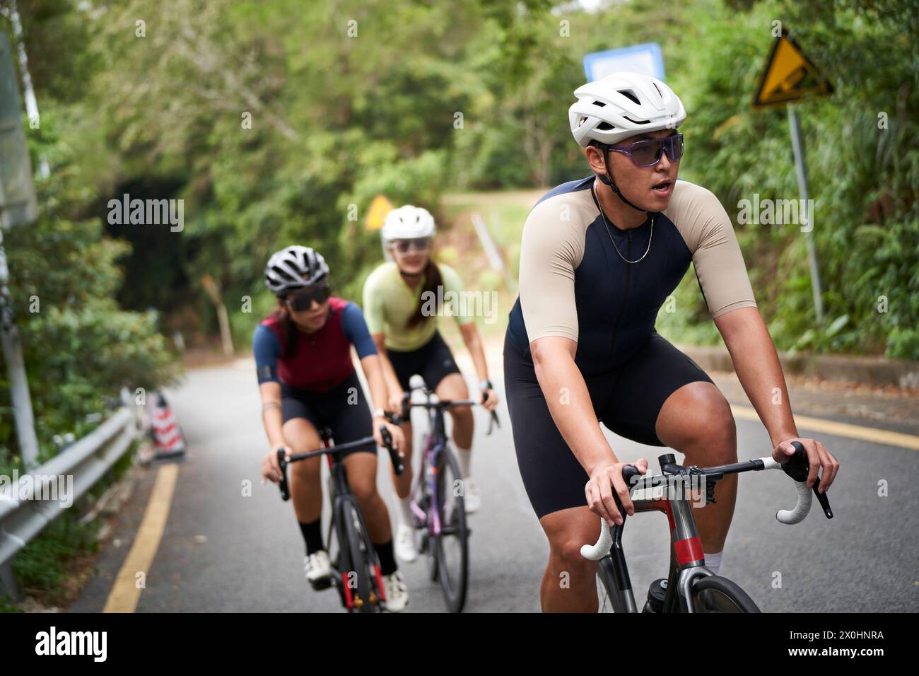 three young asian adult cycists riding bike outdoors on rural road Stock Photo