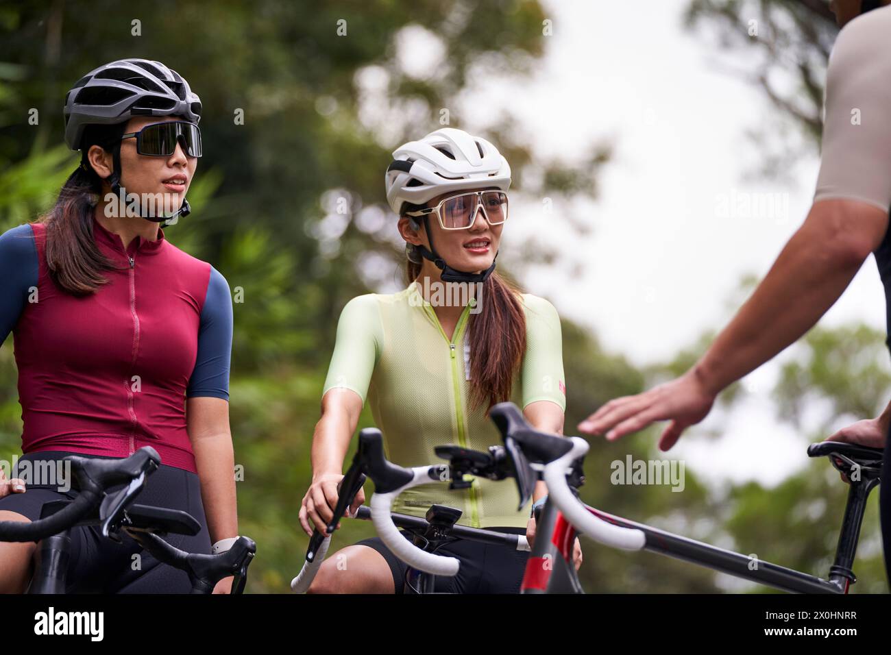 group of three happy young asian cyclists chatting conversing while riding bike outdoors Stock Photo