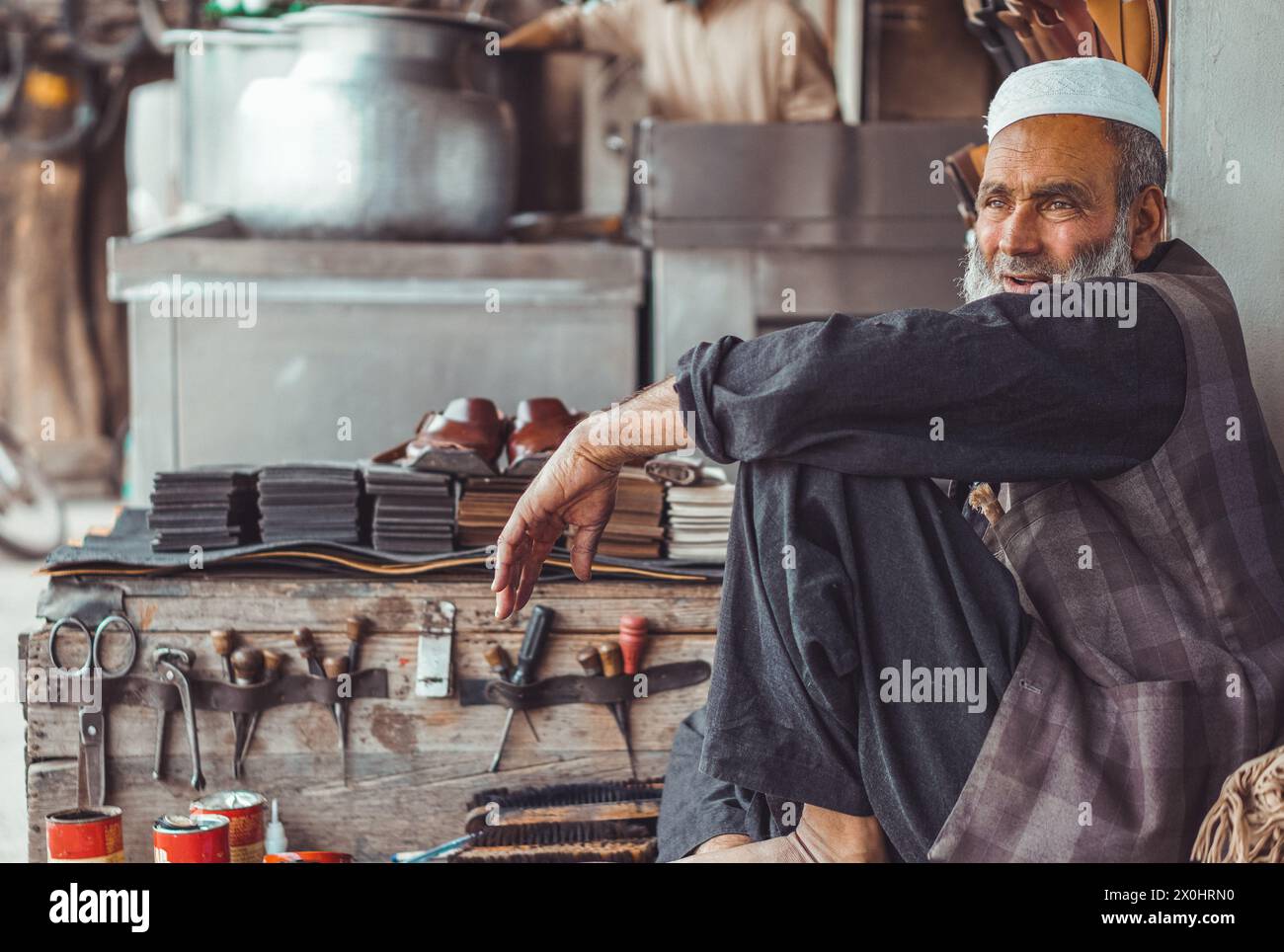 Poor old sad Pakistani Pathan shoe man cobbler on the local streets of Pakistan with his hand made leather shoes and repair tools in his street shop Stock Photo