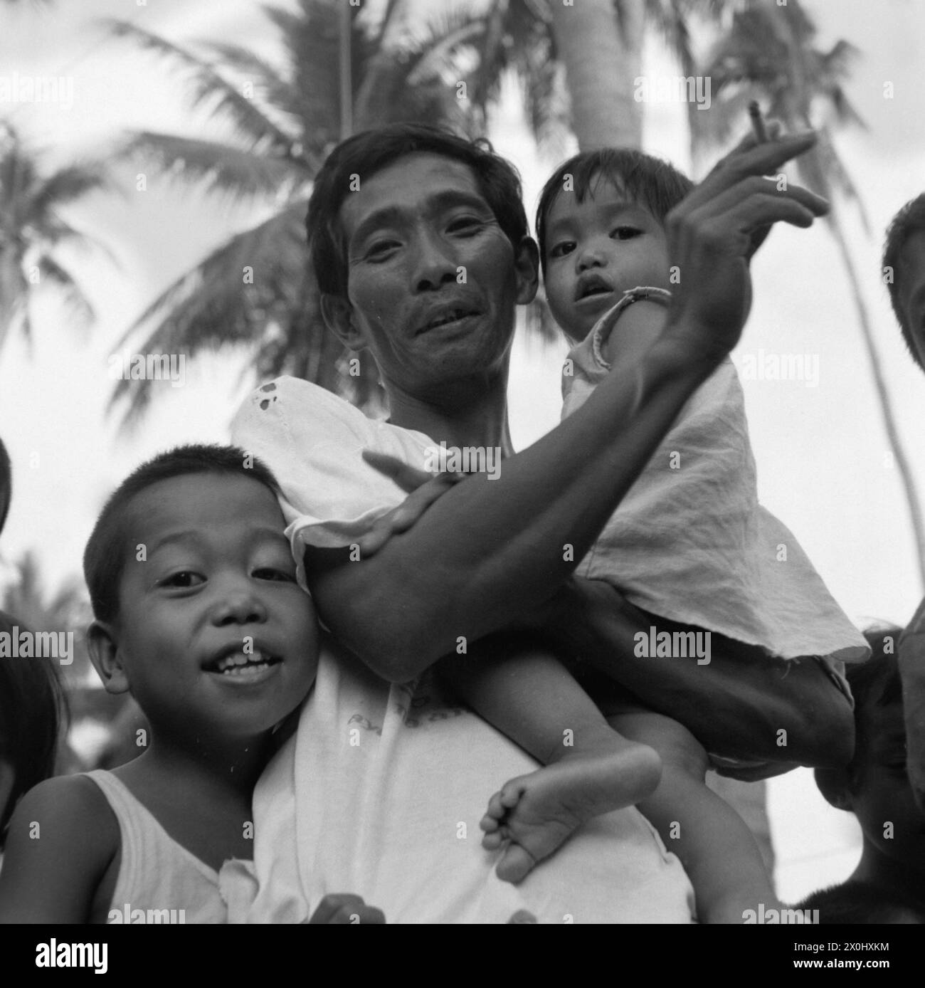 A man surrounded by children poses for a photo in Pagsanjan in the Philippines. He is holding a little girl in his arms. He smokes a cigarette. [automated translation] Stock Photo