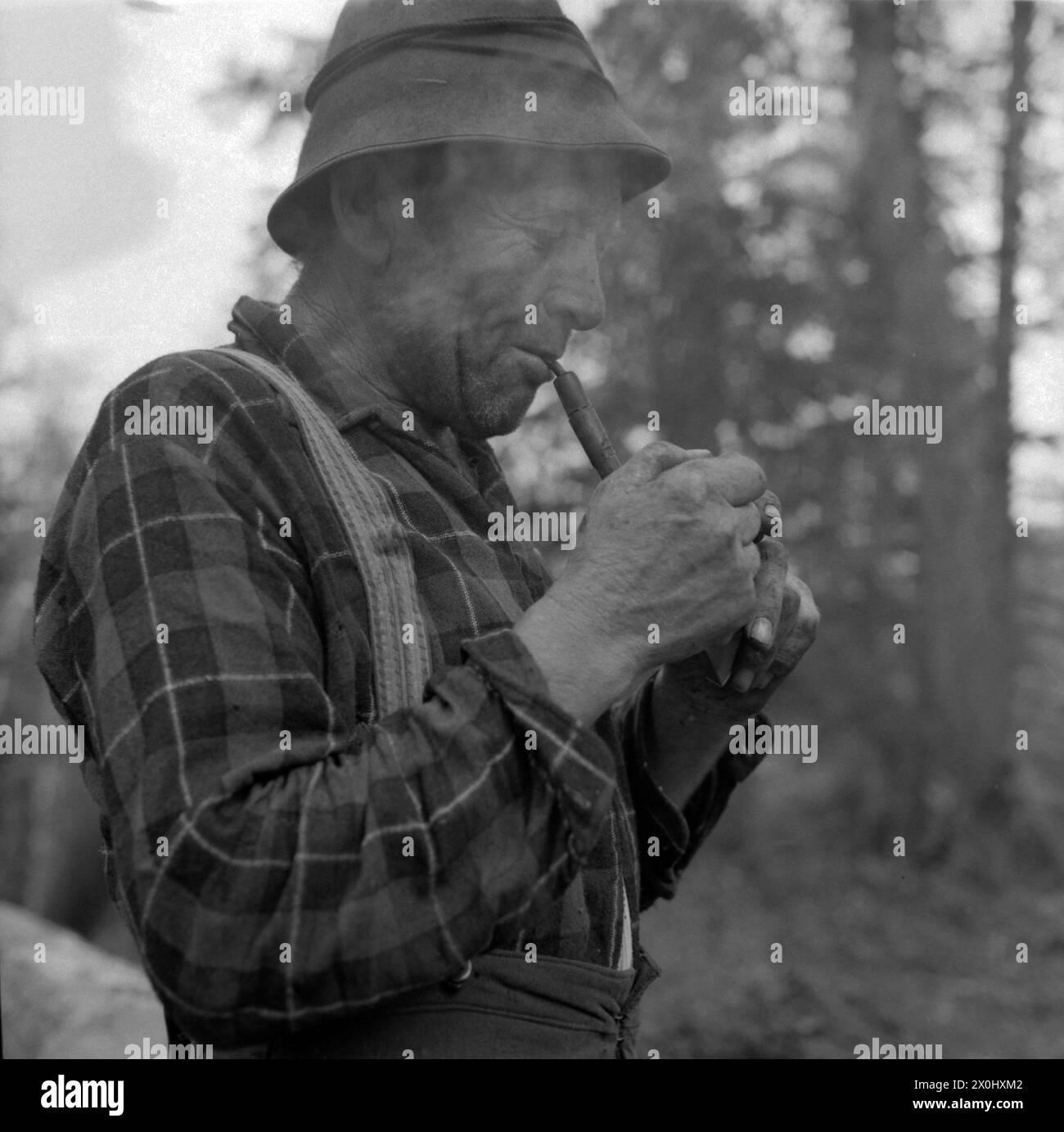 A woodcutter takes a break in the forest near Elmau near Garmisch-Partenkirchen. He lights a pipe. [automated translation] Stock Photo
