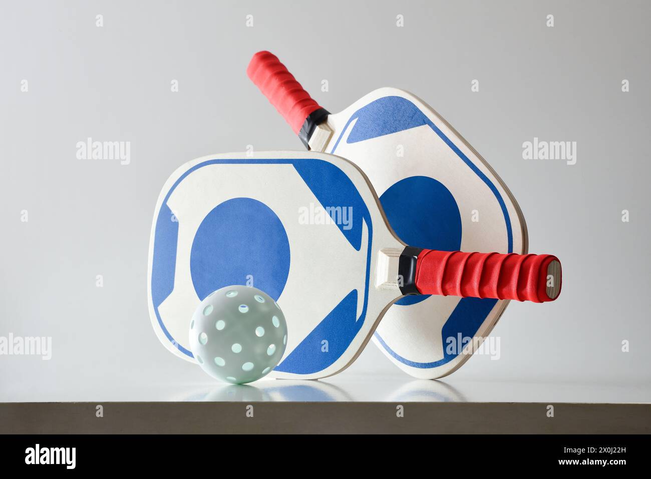 Two blue and red pickleball rackets and a white ball on white table and white isolated background. Front view. Stock Photo