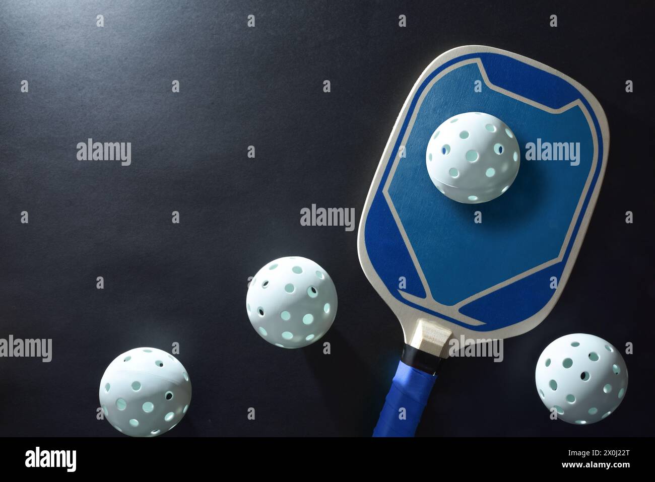 Background with blue wooden pickleball paddle and four white balls on a black table. Top view. Stock Photo