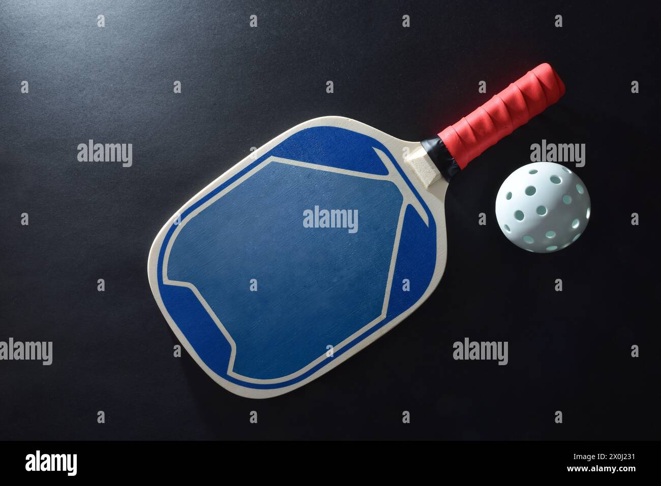 Blue and red wooden paddle pickleball racket and a white ball on black table. Top view. Stock Photo