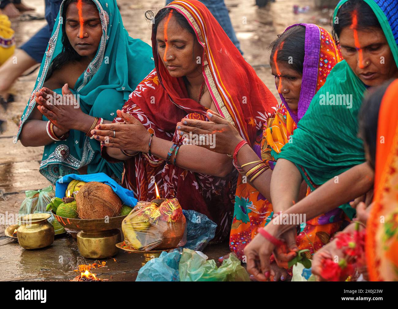 Pilgrim women with fruit offerings praying next to a flame on the banks of the Ganges River at Varanasi, India Stock Photo