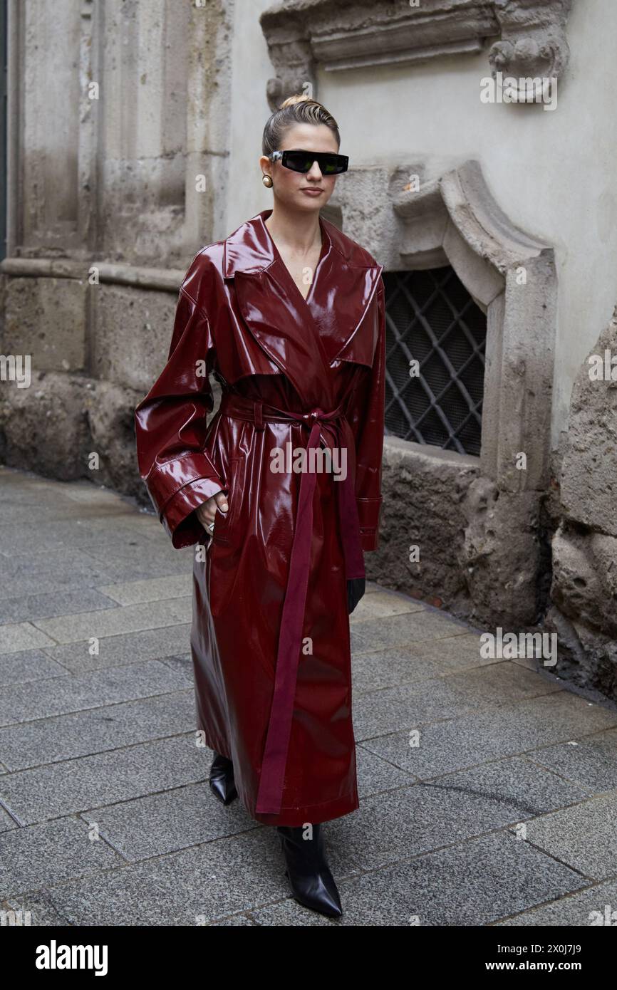 MILAN, ITALY - FEBRUARY 23 , 2024: Woman with shiny, long trench coat before Blumarine fashion show, Milan Fashion Week street style Stock Photo