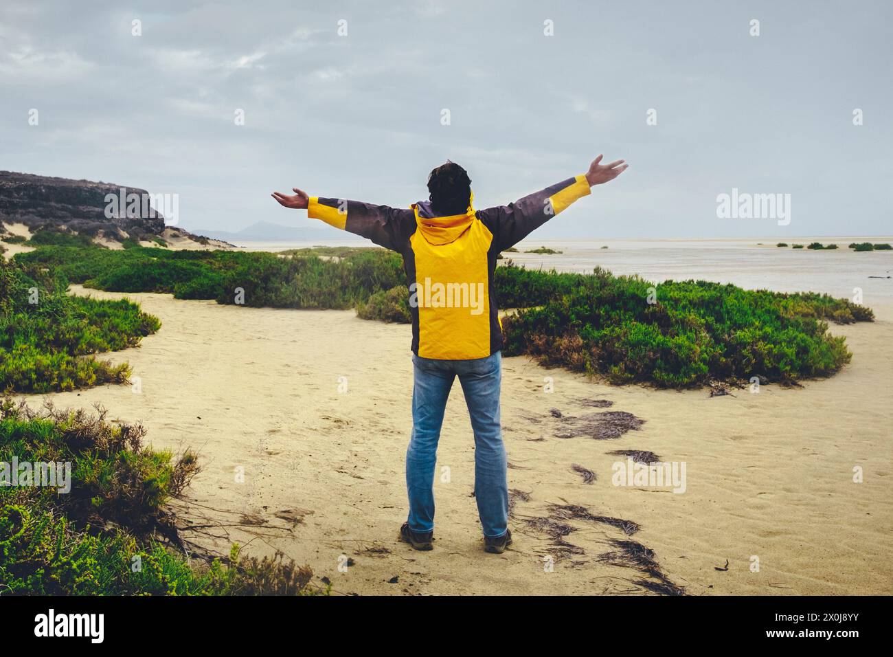 Back view of man standing and outstretching arms agains a wonderful wild landscape at the beach. Explore and adventure lifestyle people. Travel male enjoying nature Stock Photo