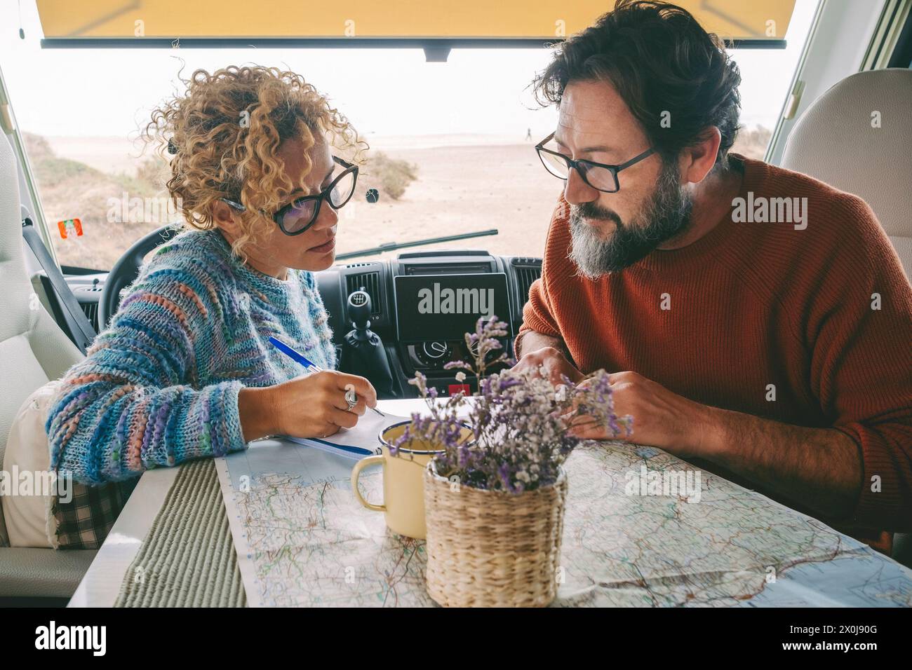 Adult couple planning next travel destination sitting inside a camper van using a paper map guide on the table. ature traveler and vanlife alternative people lifestyle. Couple of tourist and beach view Stock Photo