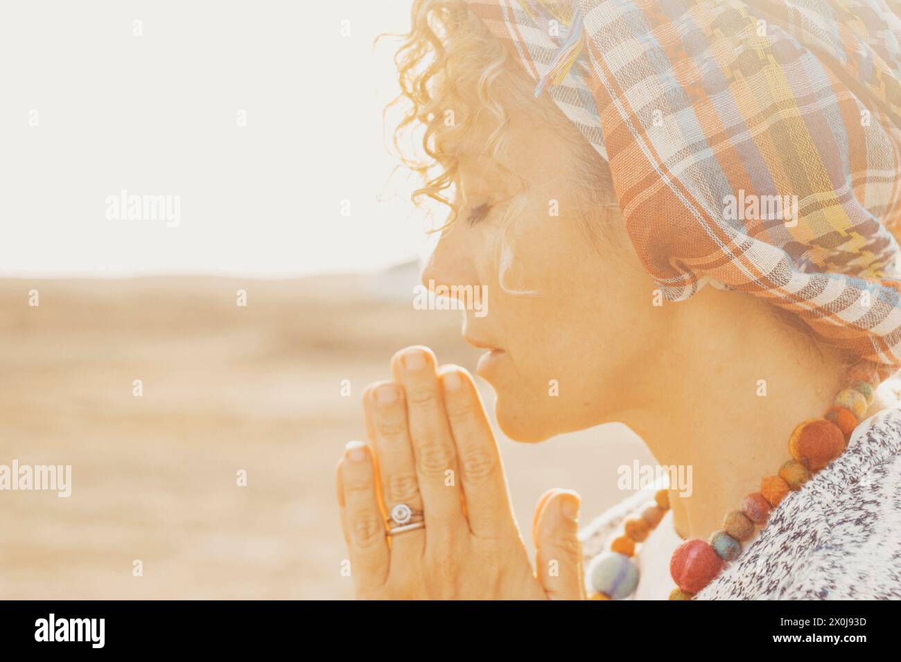 Portrait of woman with joyned hands and closed eyes pray and maditate outdoors with bright sunlight in background. Concept of meditation and inner balance life. Stock Photo