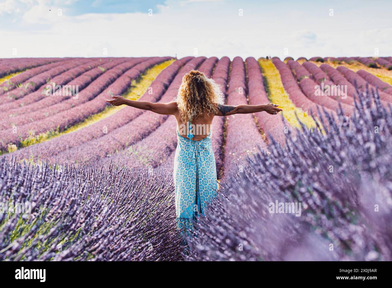 Happy and free traveler woman outstretching arms and enjoy amazing nature landscape in the middle of a violet lavender field flowers scenic destination. Concept of people and travel lifestyle Stock Photo