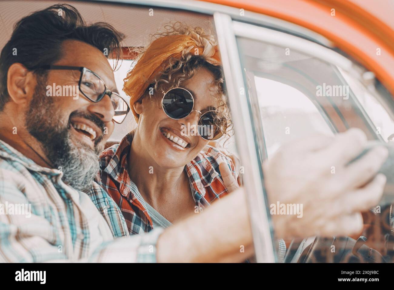 Happy couple having fun inside a car during travel adventure. Cheerful man and woman smiling and laughing a lot together. People enjoying vehicle trip in friendship and relationship. Concept of drive Stock Photo