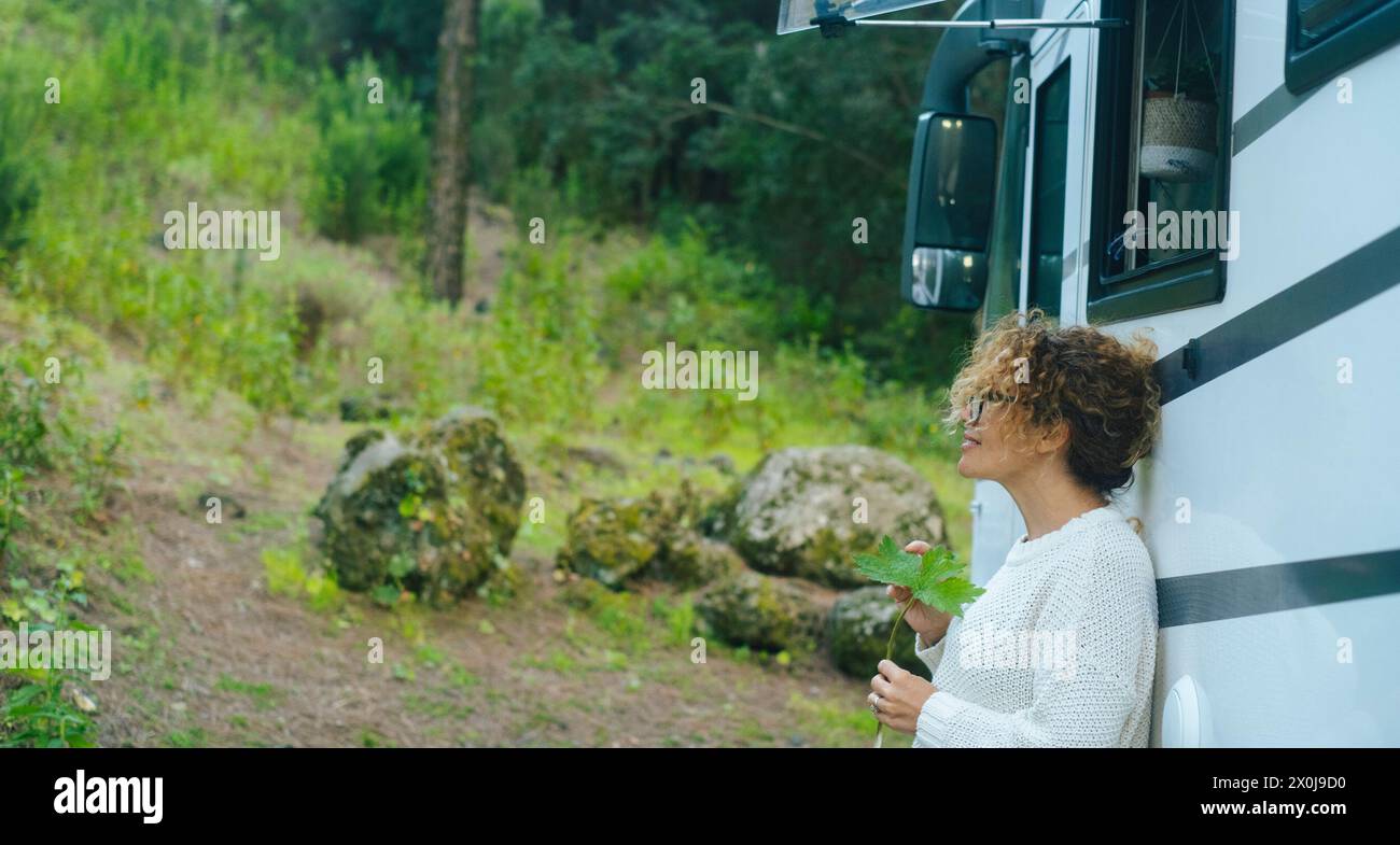 One serene woman enjoy relax and calm outdoors standing outside a camper van and admiring green nature forest around. Travel destination and vehicle journey adventure vacation lifestyle. Happiness Stock Photo