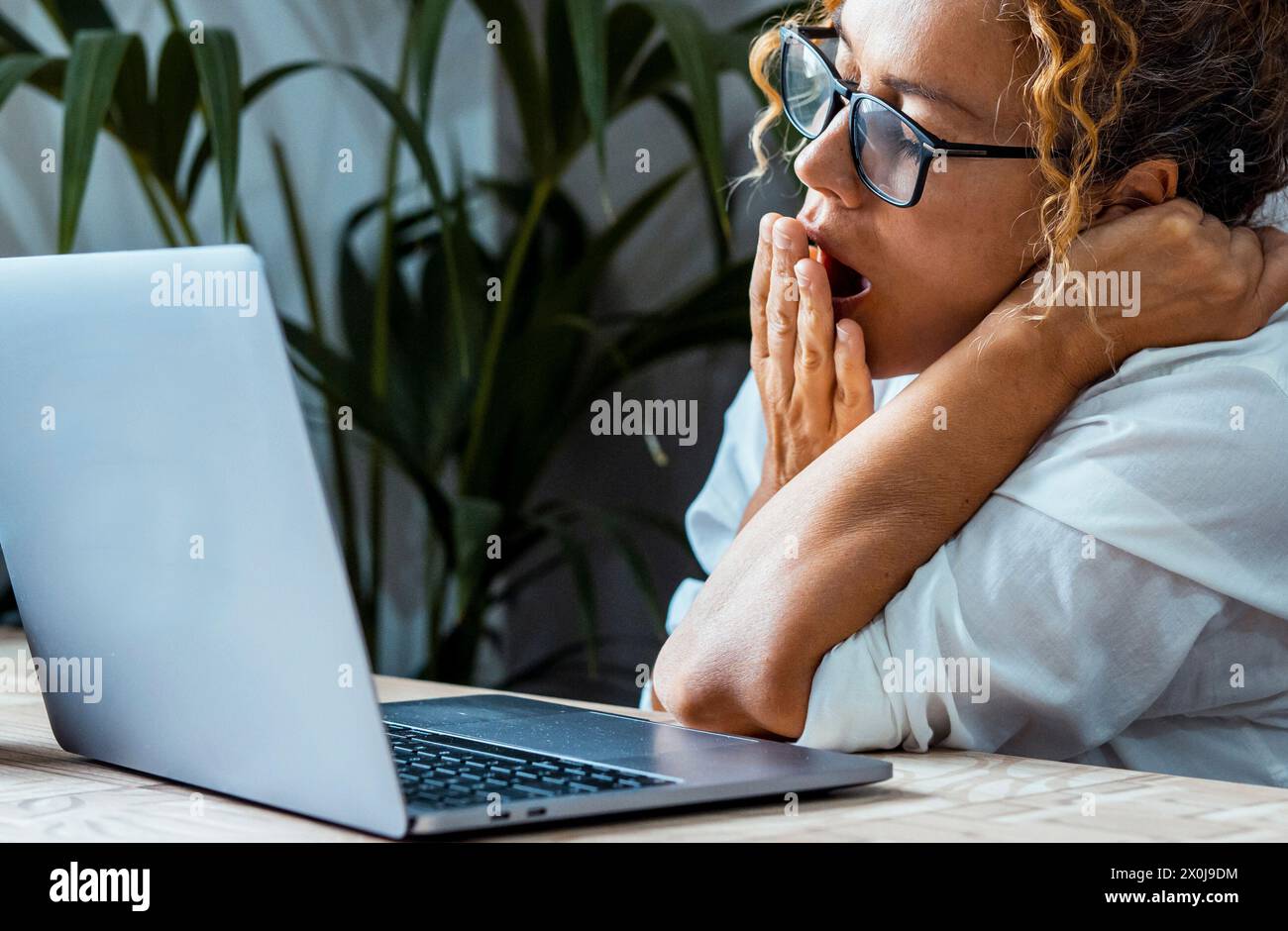 One woman doing yawn for tired and bored condition in front of an open laptop at the desk. Smart working online business and freelance lifestyle. Exhausted female people overwork use computer office Stock Photo