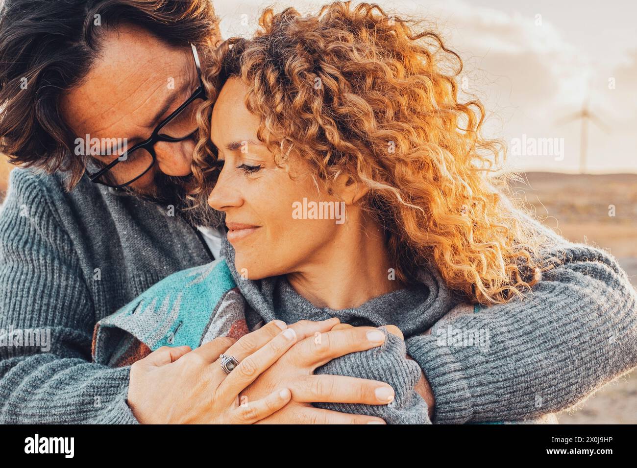 Love and travel people together. One man hug woman from behind in romantic outdoor leisure activity together. Desert scenic landscape in background with windmills and sunset time. Adventure traveler Stock Photo