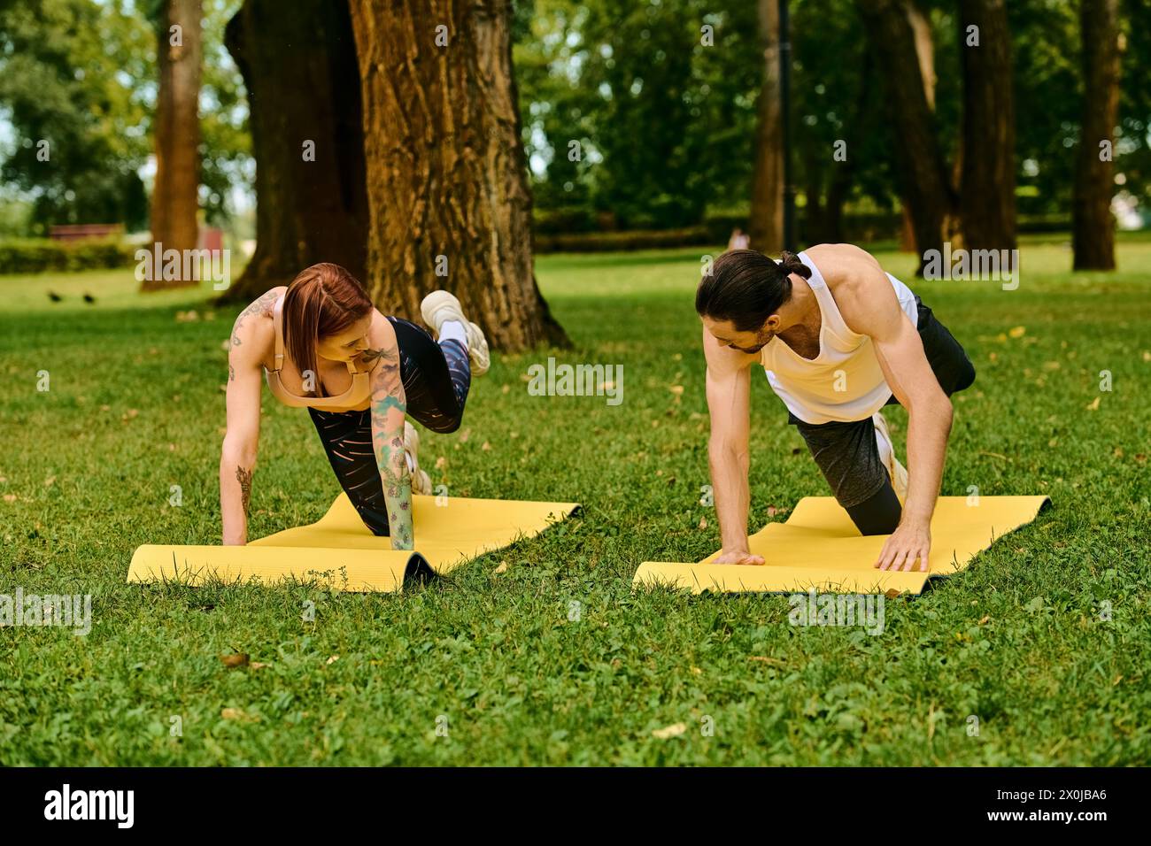 A man and woman in sportswear engage in partner yoga poses with determination and motivation during an outdoor session. Stock Photo