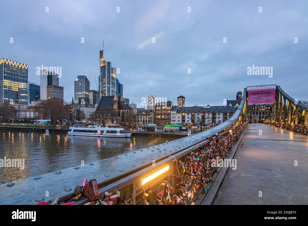 The pedestrian bridge, iron footbridge with love locks on the railing, sunset with a view of the skyline of the financial district of Frankfurt am Main, Germany Stock Photo