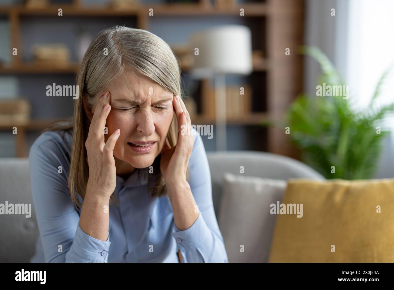 A mature woman sits in her living room, visibly distressed with a ...