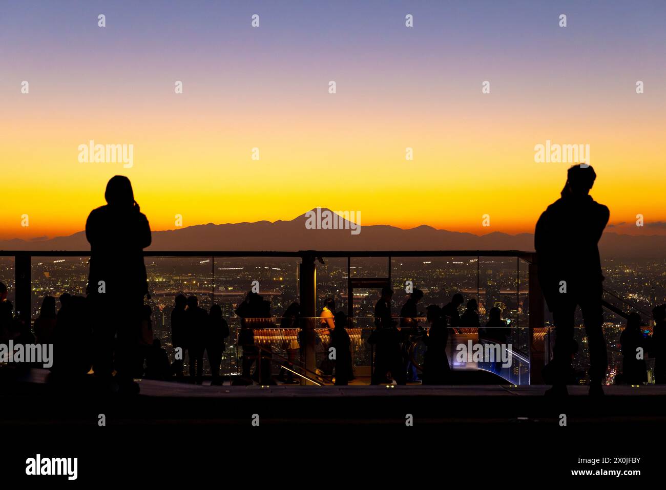 People admire Tokyo cityscape against a vibrant sunset, with Fuji mountain silhouette horizon Stock Photo