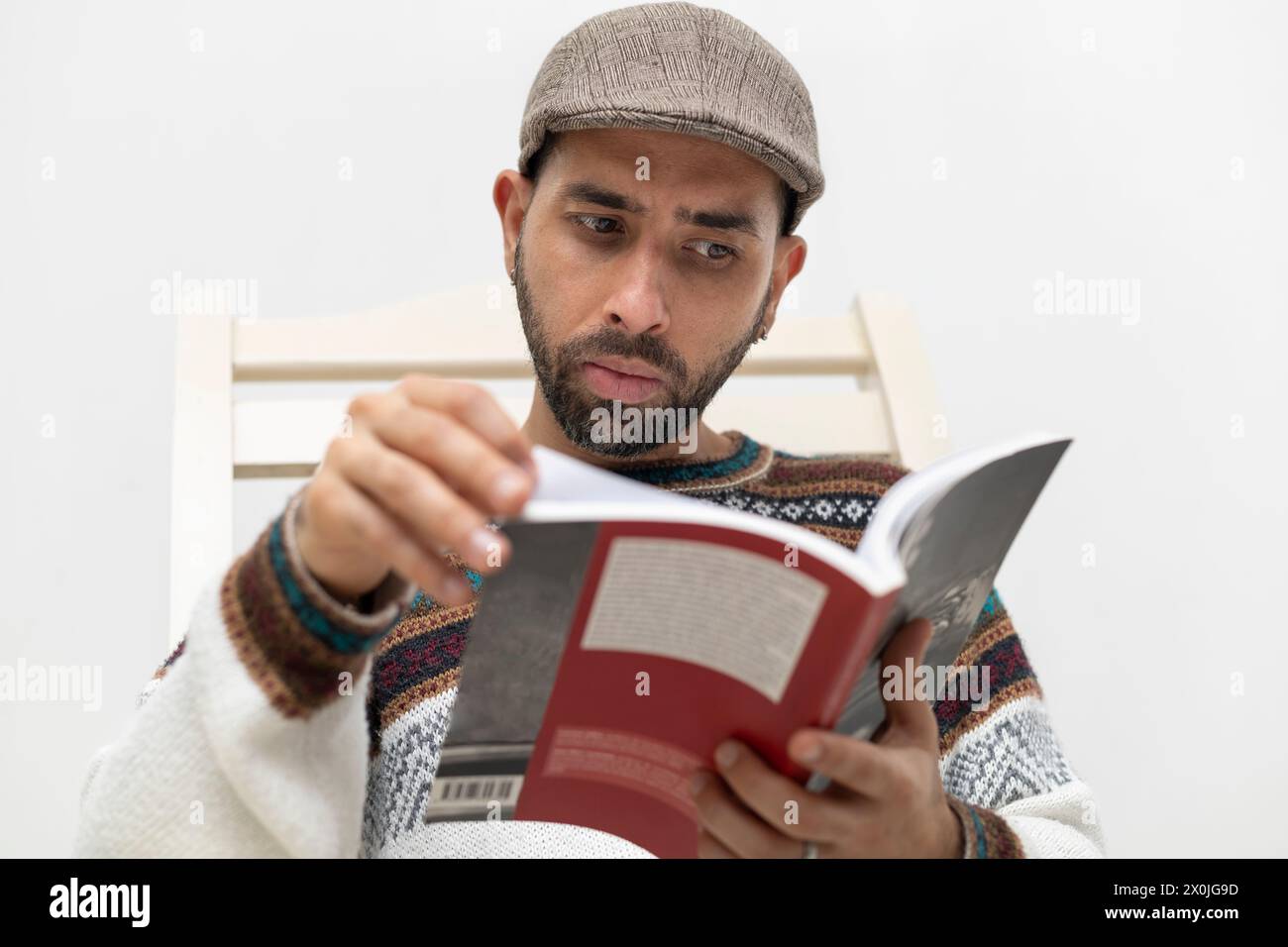 Latin American man sitting in a chair in his house reading a book Stock Photo