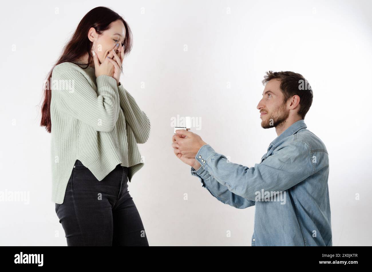 Man on his knees proposing marriage to his girlfriend with a ring box in his hands Stock Photo