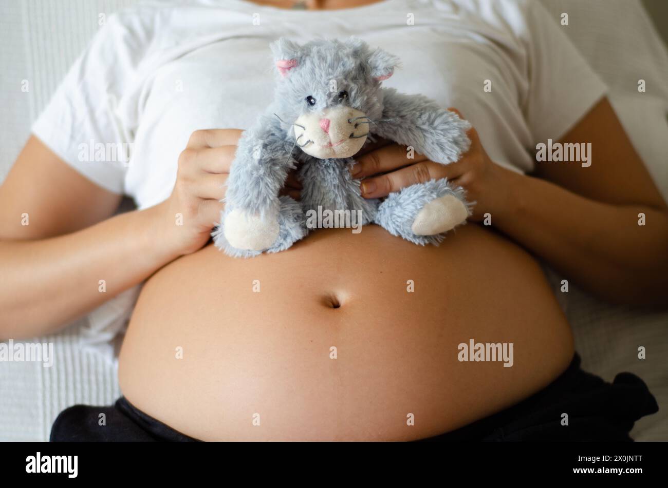 Pregnant woman holding a stuffed animal in her belly Stock Photo