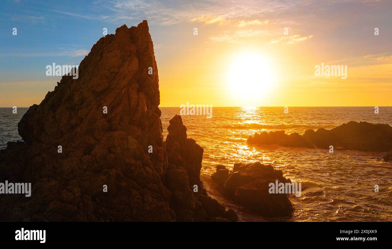 A Stunning Seascape at Sunset with a Rocky Coastline, Creating a Serene and Majestic Contrast Against the Setting Sun, Illuminating the Horizon. Stock Photo