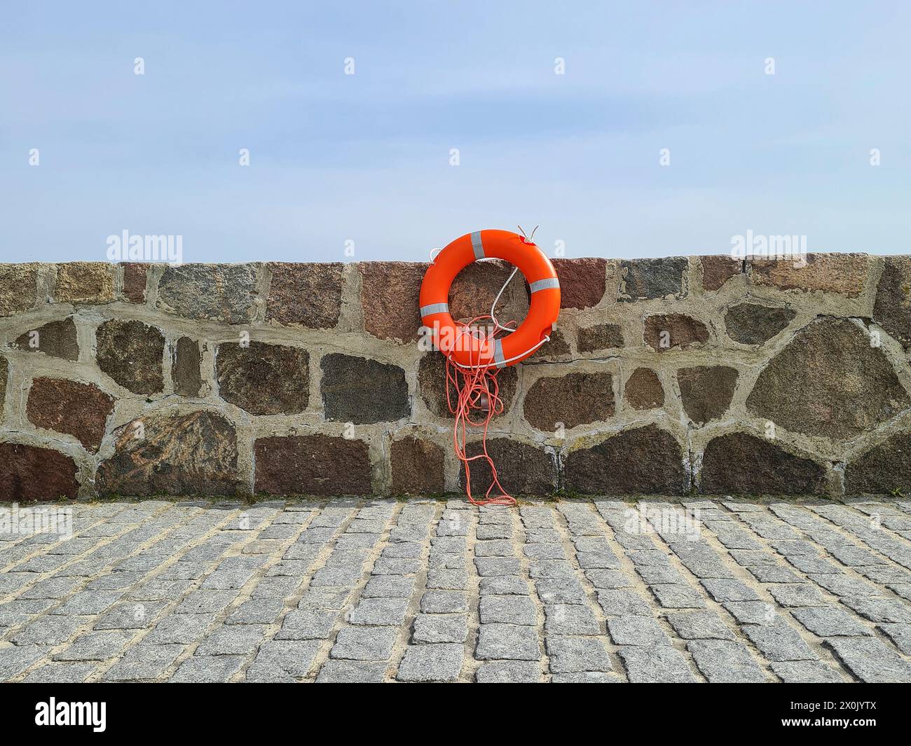 A lifebuoy with 4 reflective strips is attached to a stone wall, in the foreground are cobblestones, Baltic Sea, Germany Stock Photo