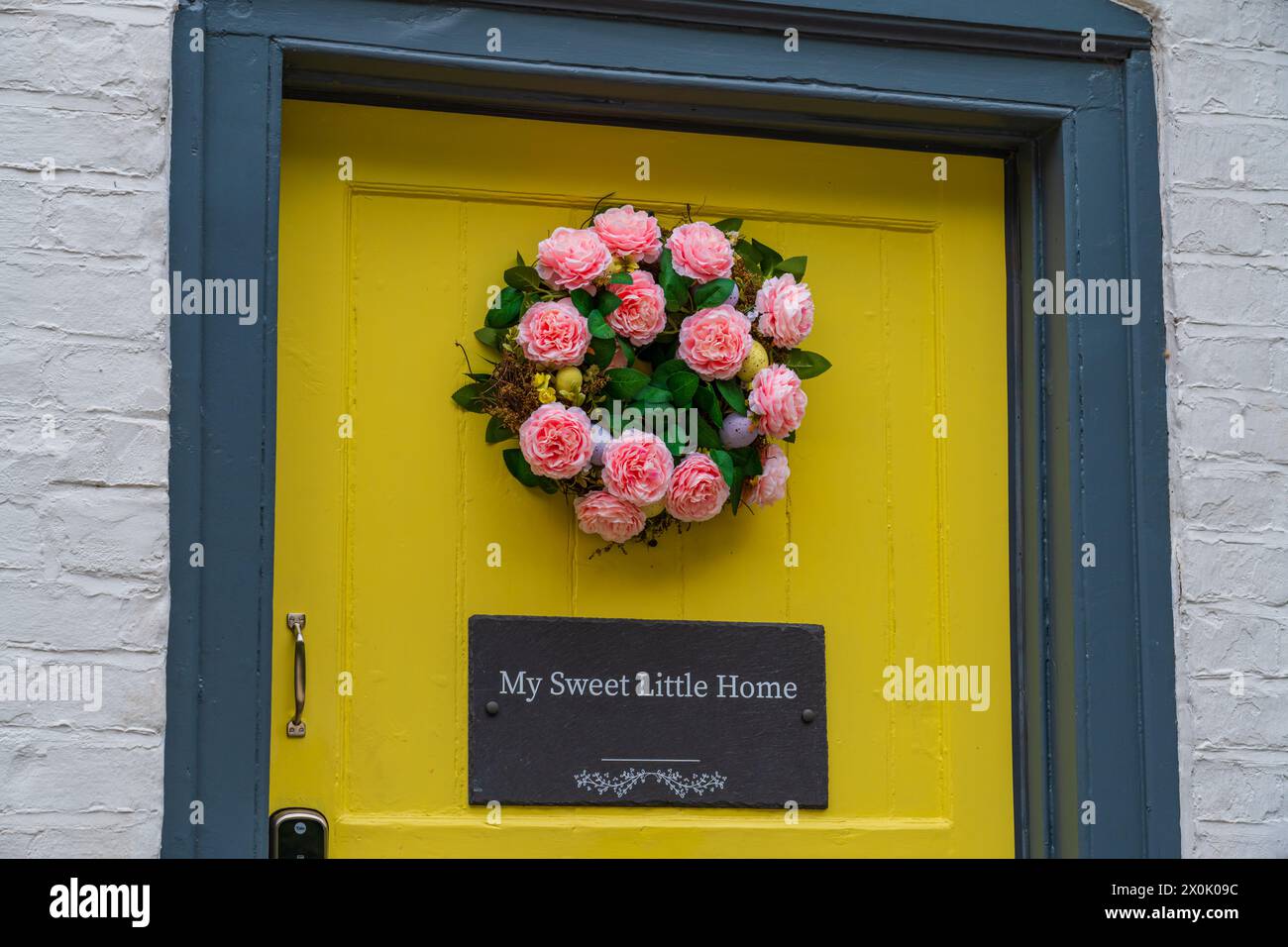 Yellow front door with a plaque title 'My sweet little home' and a pink coloured rose wreath Stock Photo