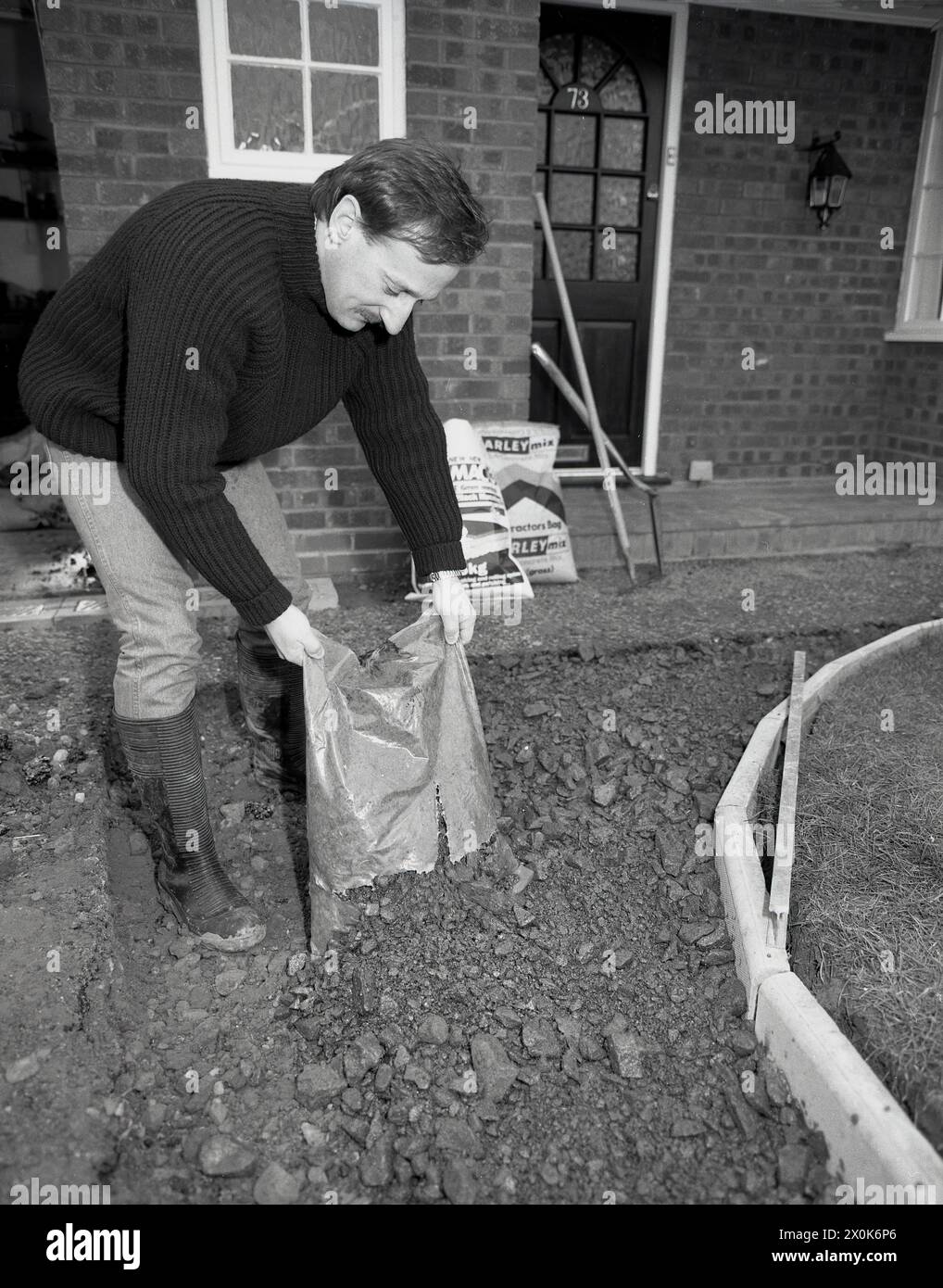 1980s, a man building a new driveway outside a house, putting down hard core rubble as a base. Hardcore is an essential material to lay strong foundations for any building works. Stock Photo