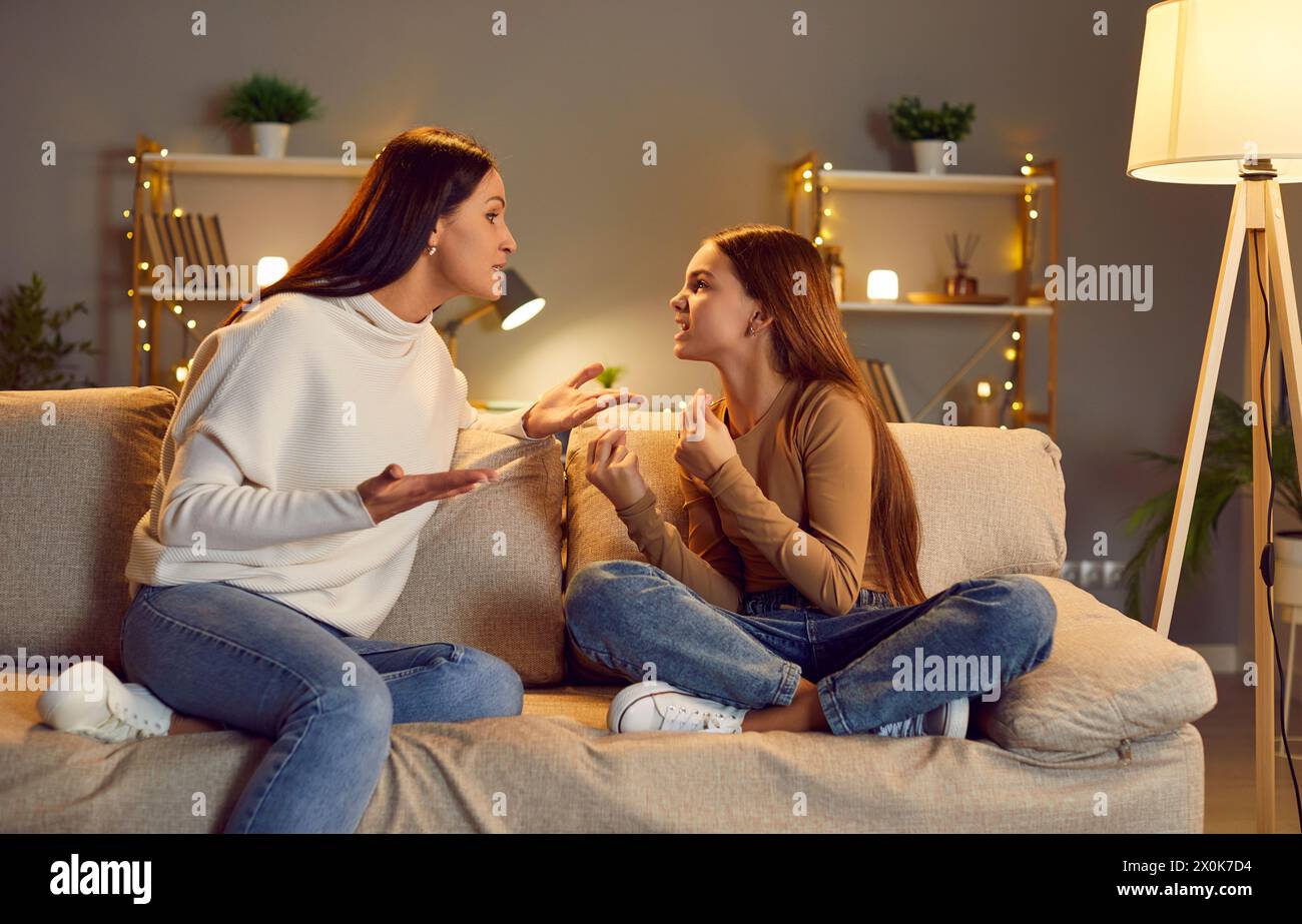 Annoyed emotional mother arguing and quarreling with her child sitting on sofa at home. Stock Photo