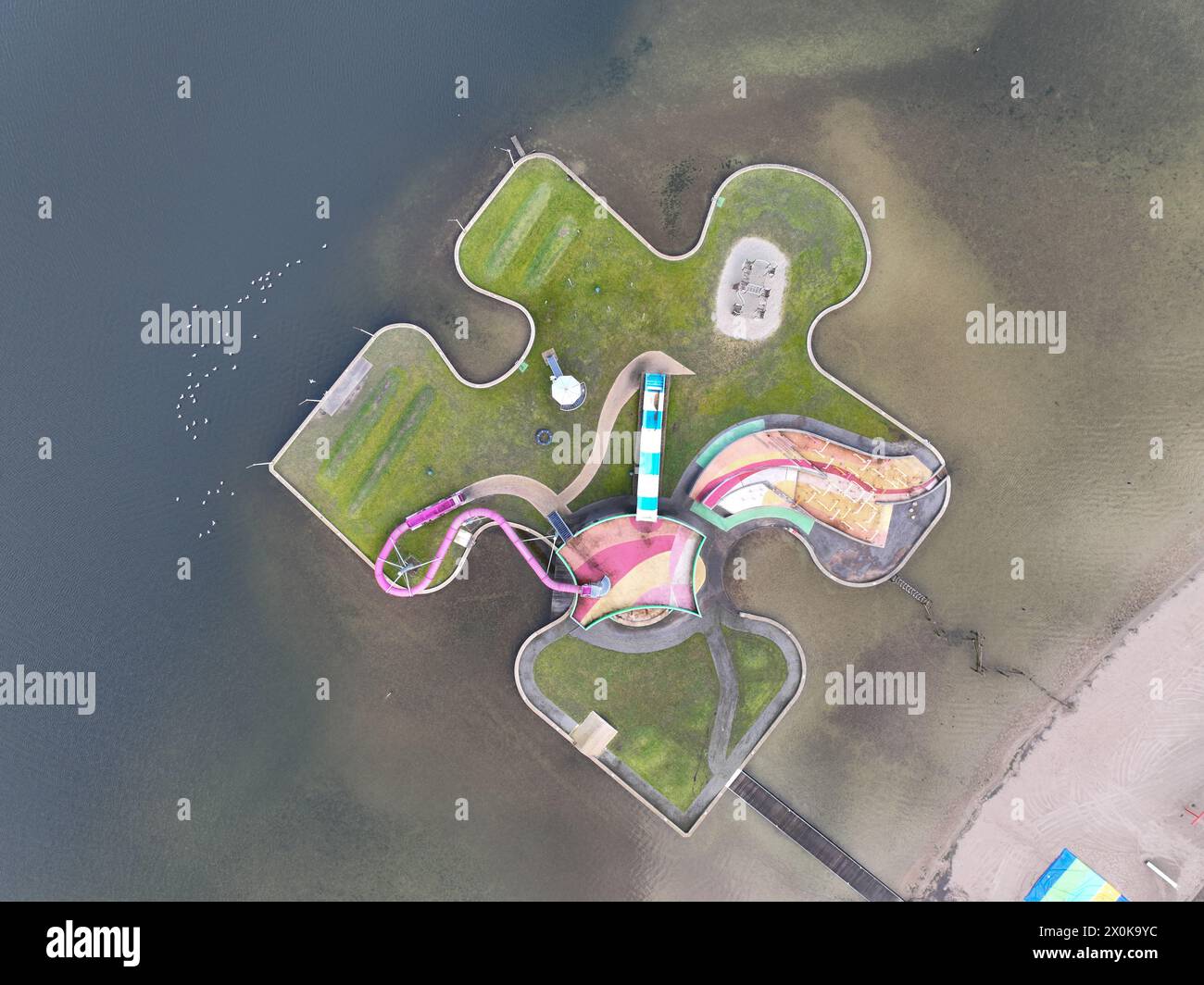 Children recreational playground, playfull colors, climbing rack, slide and other attributes on a puzzle piece on water. Aerial drone view. Stock Photo