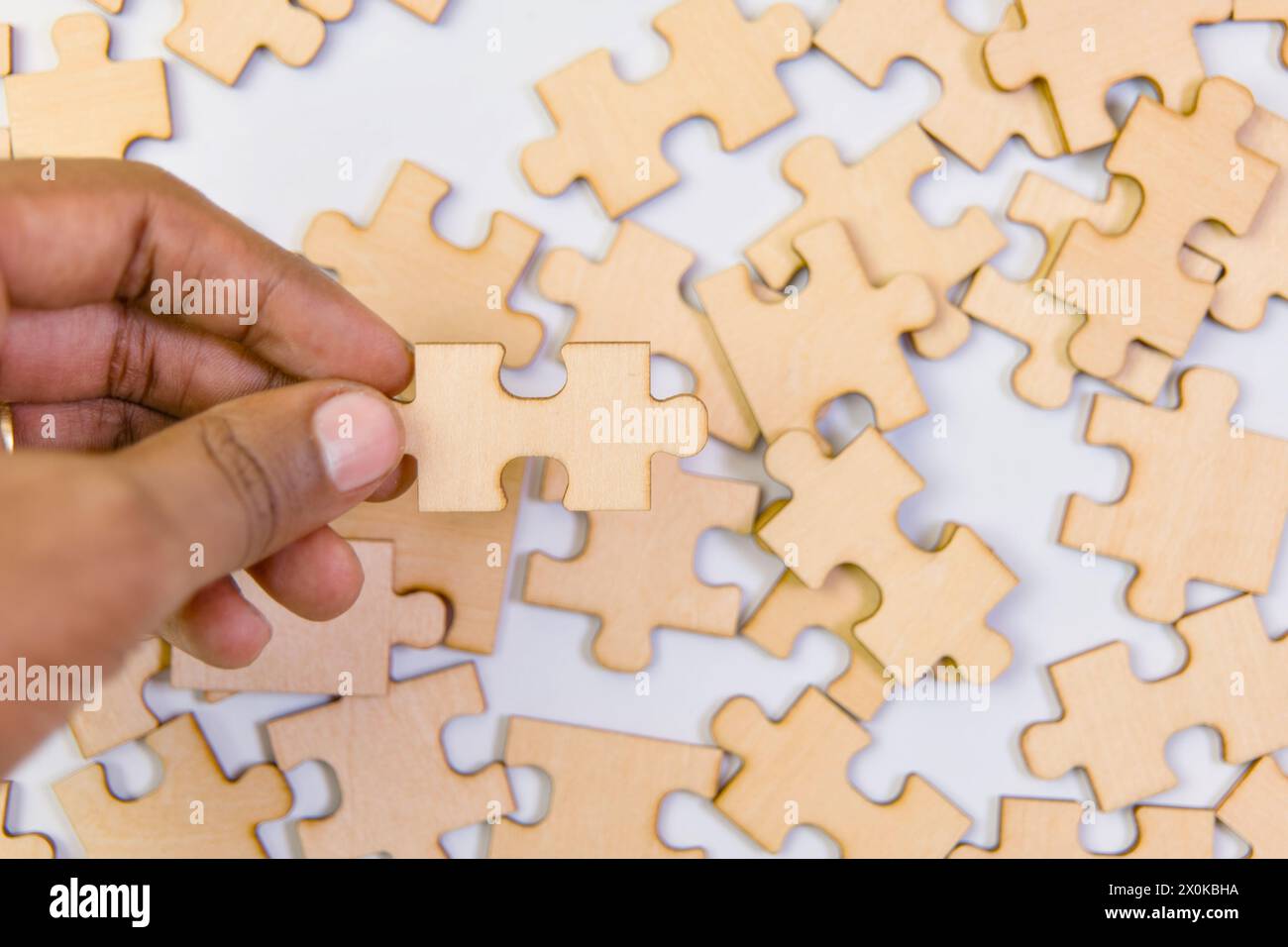 Close up of human hand putting jigsaw puzzle piece on white background Stock Photo