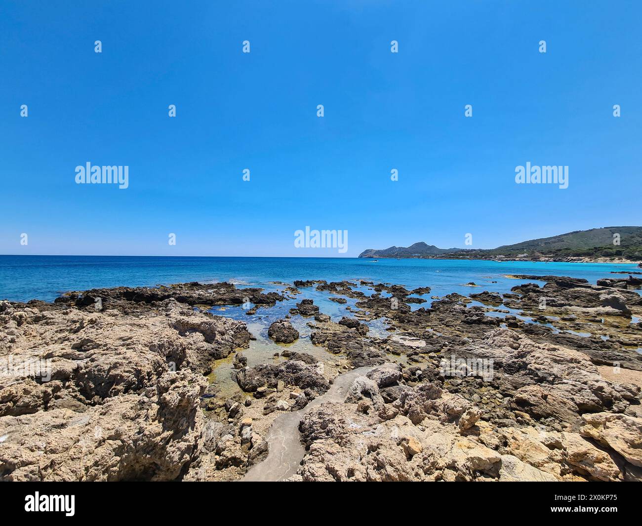 View over the rocks in the foreground to the turquoise water on the promenade of Cala Ratjada on a beautiful summer's day, Mallorca, Spain Stock Photo