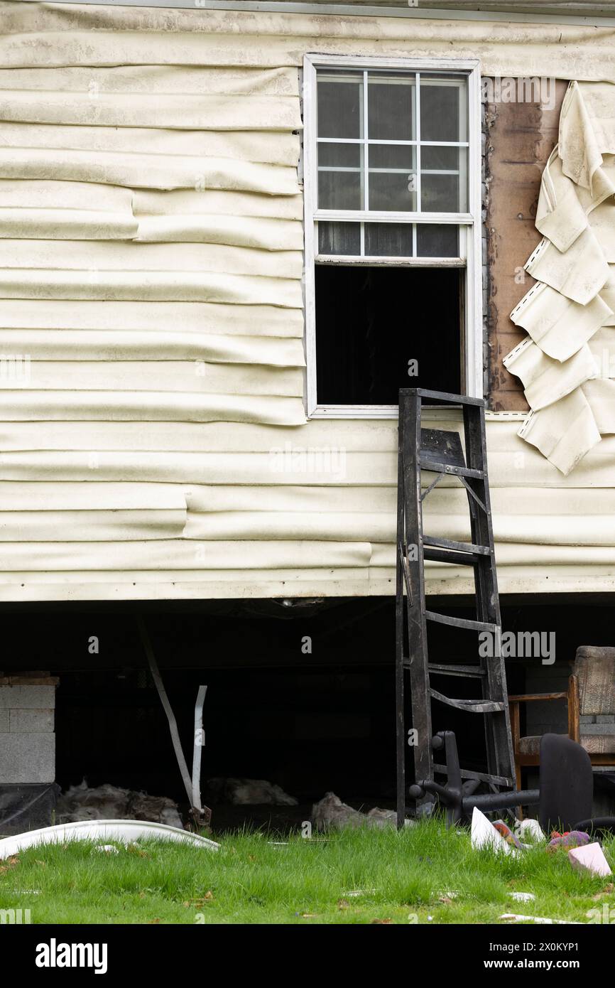 An open exterior window with damaged and melted plastic vinyl siding covered in dirty soot on a home that had a hot heat interior fire. Stock Photo