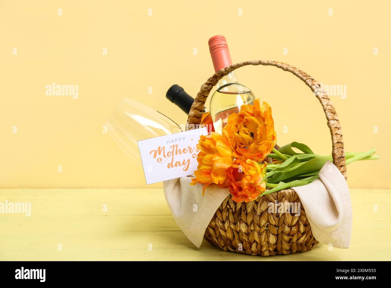 Basket with bottles of wine, glass and tulip flowers for Mother's Day celebration on color wooden table Stock Photo