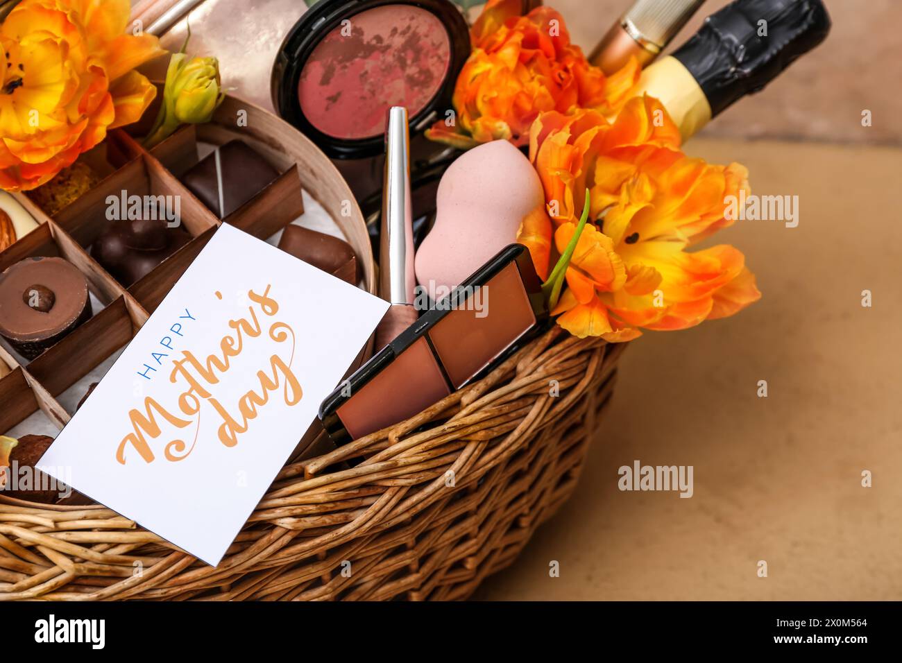 Gift basket with candies, cosmetics and tulip flowers for Mother's Day celebration on color table, closeup Stock Photo