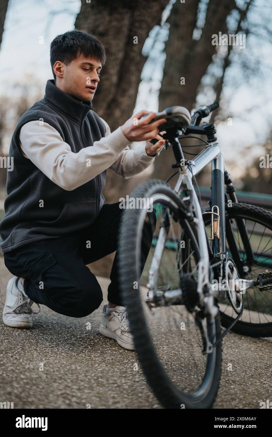 Casual teenager boy with bicycle in park setting adjusting bike seat ...