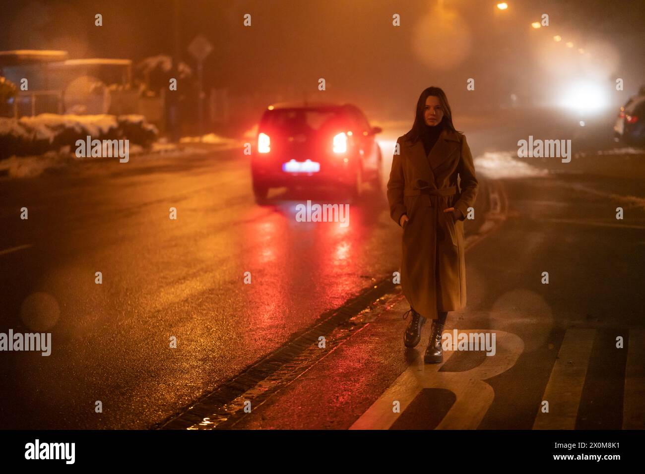 Young woman in a long coat standing by a road. Stock Photo