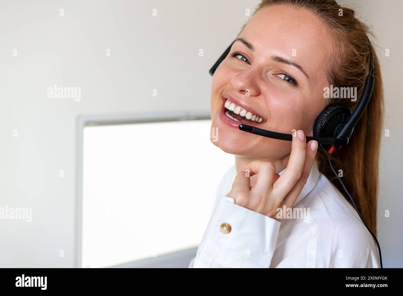 Happy employee in office. Woman customer service agent in headset looking at camera and smiling. Stock Photo